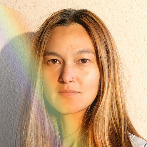 Woman with long hair, gazing directly into camera, with a ray of light beaming on her face